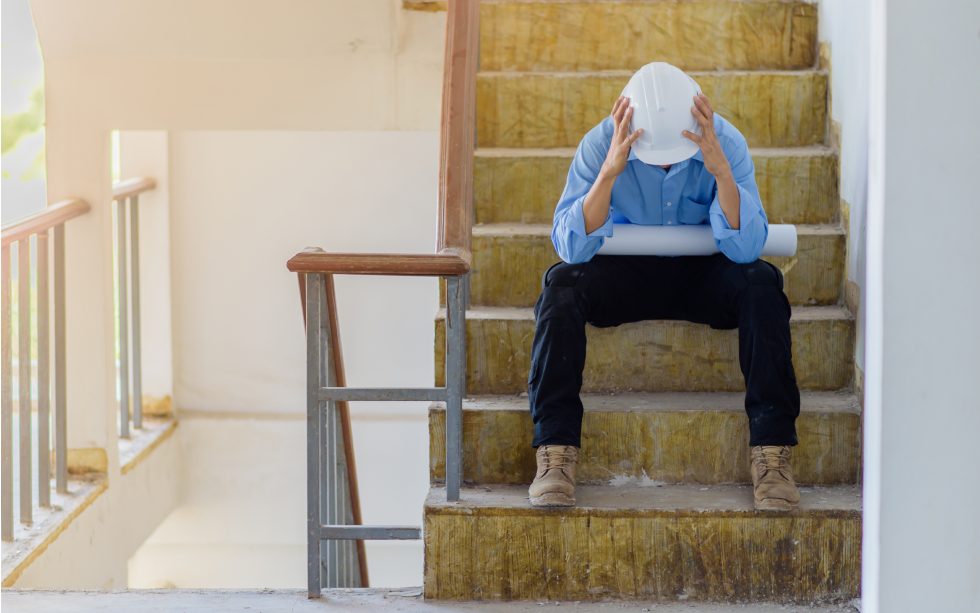 dělník v přilbě sedící na rozestavěném schodišti